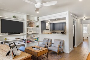 Un salon moderne doté d’un téléviseur à écran plat, de deux fauteuils gris, d’une table basse en bois et d’un ventilateur de plafond.