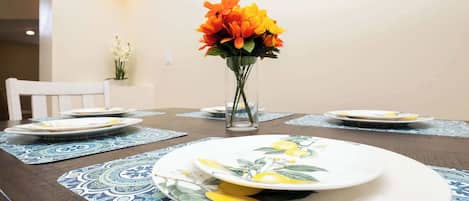 Une table à manger dressée avec des assiettes, un vase de fleurs et des sets de table à motifs.