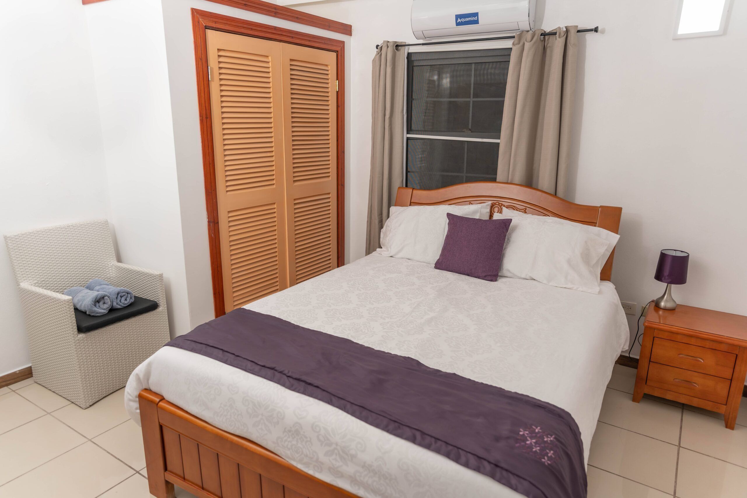 Un dormitorio ordenado con cama, una silla, armario y mesita de noche.