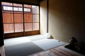 A tatami mat room with a shoji screen door, a white cushion, and a traditional Japanese tea set. - Honmachi-Shin North (Kyoto)