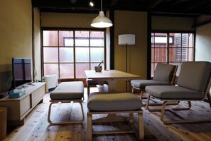 A room with a wooden floor, a table with chairs, a television, and a window with a view. - Honmachi-Shin North (Kyoto)