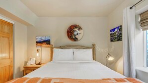 A bedroom with a bed, a nightstand, a lamp, and a wall with two paintings.