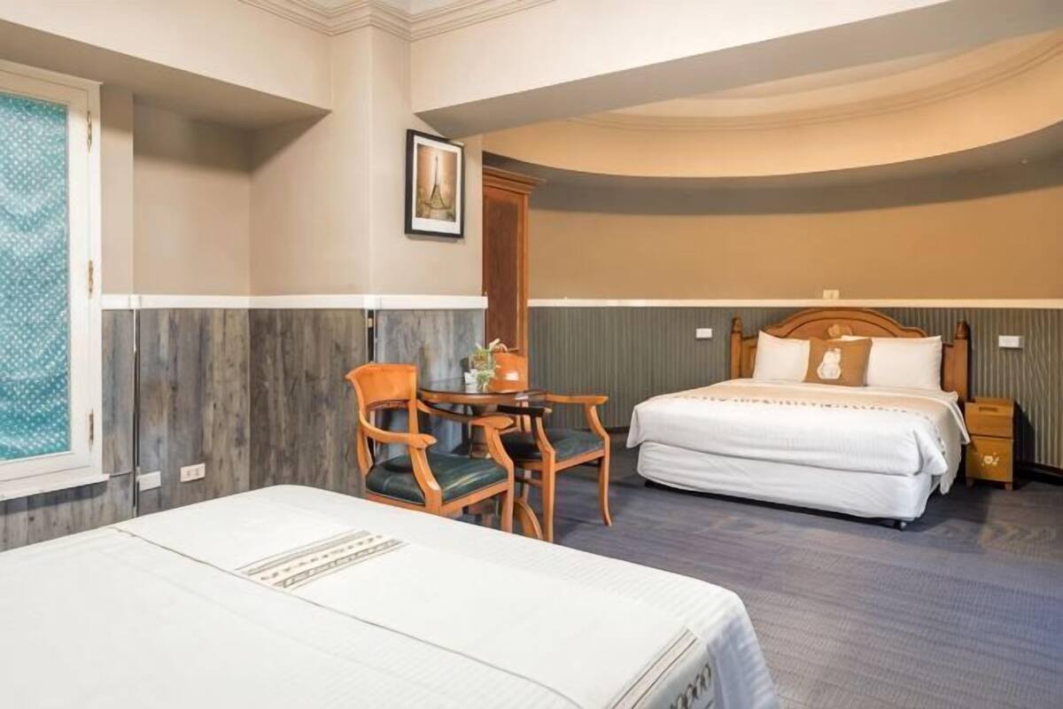 Habitación de hotel con cama, escritorio con silla, mesita de noche y ventana con vistas.