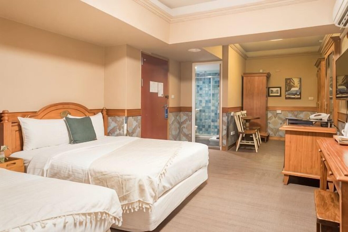 Ett hotellrum med två sängar, ett skrivbord, en stol och ett badrum som syns genom en öppen dörr.