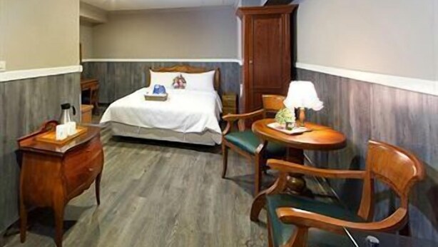 A hotel room with a bed, a desk with a lamp, a chair, and a wardrobe. - Hotel de Trianon (Taitung)