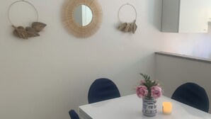 A dining area with a white table, two blue chairs, and a vase with flowers. - Charming 2-bedroom condo with AC, WiFi just Steps from the Beach (Anzio)