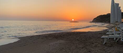 Una spiaggia al tramonto, con una riva sabbiosa e una fila di sdraio bianche.