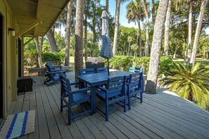Una terraza cubierta al aire libre con mobiliario azul, una parrilla y un paraguas estampado.
