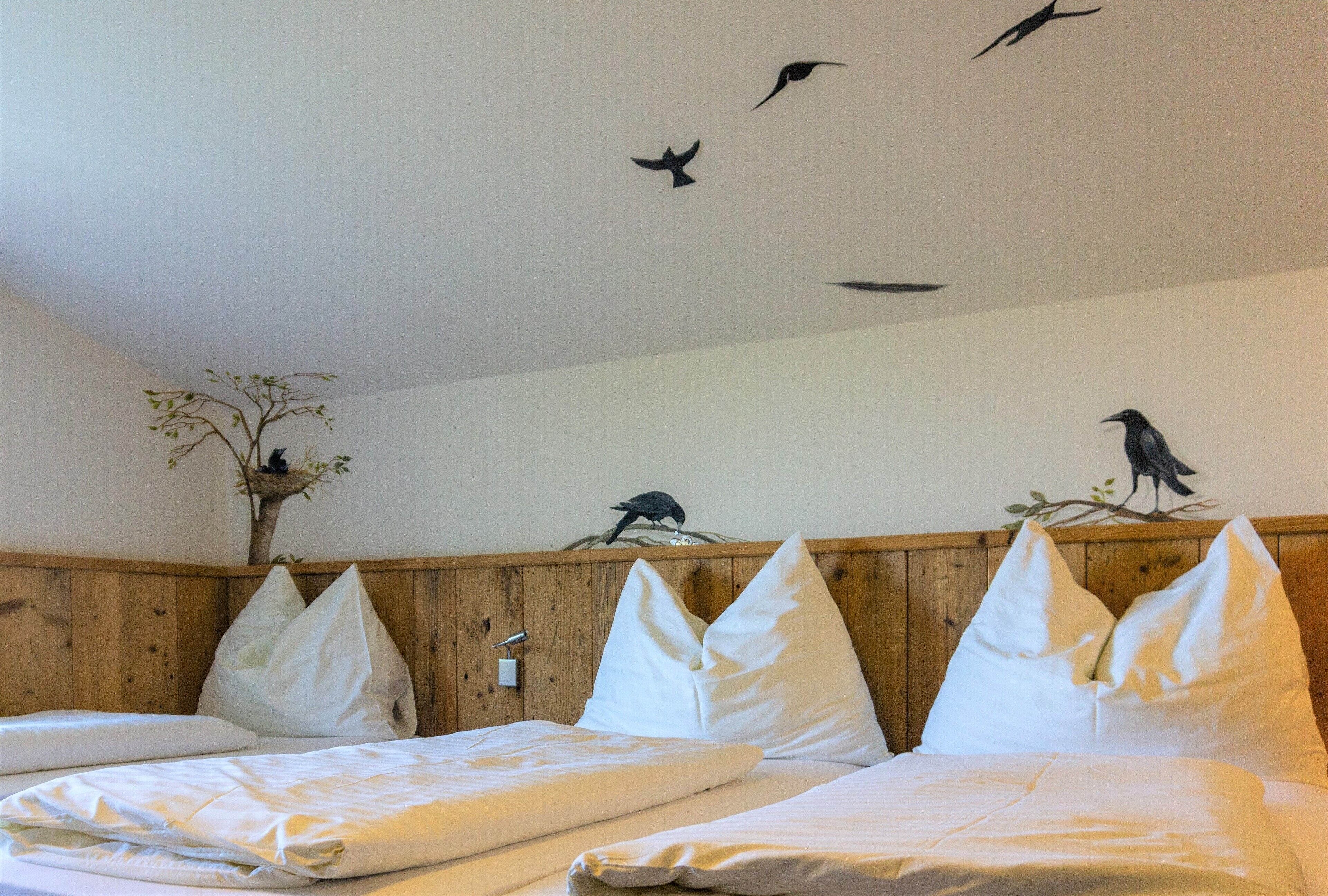 Een hotelkamer met twee bedden, een houten hoofdeinde, wit beddengoed en een wanddecoratie van vogels.