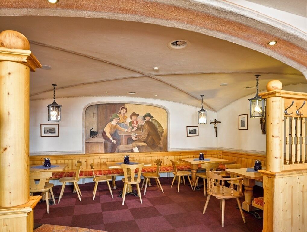 Un restaurante con bancos y mesas de madera, un mural en la pared y lámparas colgantes tipo farol.
