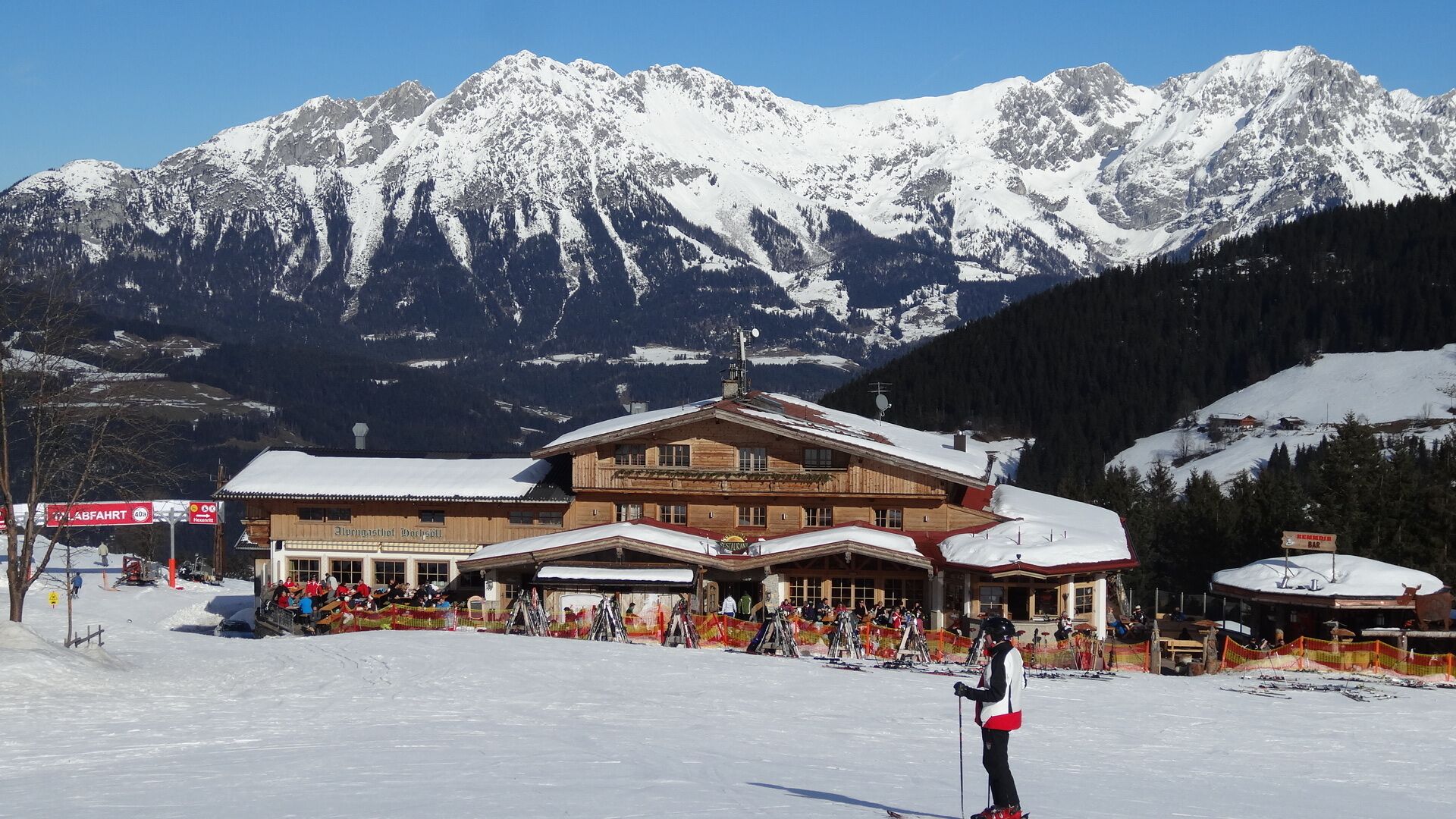 Une station de ski avec un bâtiment en bois, des pistes de ski et, en arrière-plan, des montagnes enneigées.