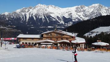 Une station de ski avec un bâtiment en bois, des pistes de ski et, en arrière-plan, des montagnes enneigées.