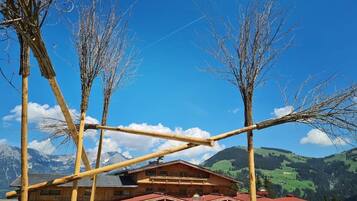 Un edificio de madera con techo inclinado, rodeado de sombrillas rojas, con montañas y cielo azul despejado de fondo.