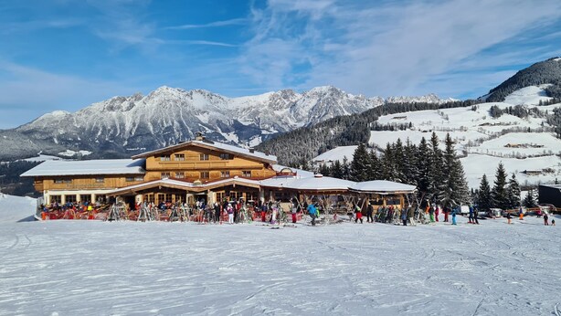A wooden lodge with a ski slope in the foreground and snow-covered mountains in the background. - Alpengasthof Hochsöll (Soell)