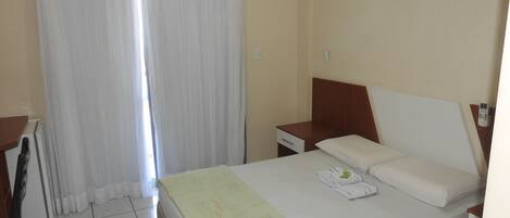 A hotel room with a bed, a bedside table, a chair, a window with curtains, and an air conditioning unit.
