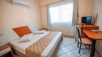 A hotel room with a bed, a desk with a computer, a chair, and an air conditioning unit.