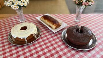 A table with a red and white checkered tablecloth, two cakes on metal plates, and two vases with flowers.