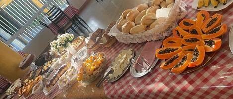 Mesa de buffet com diversos alimentos, incluindo pão, doces e frutas.