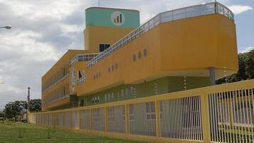A modern building with a yellow facade, a clock tower, and a fenced area with small plants.
