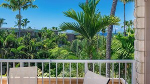 A balcony with a view of a lush garden and a building in the background.