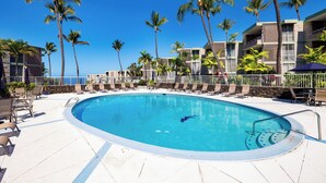 A swimming pool with lounge chairs and palm trees, surrounded by a building with balconies.
