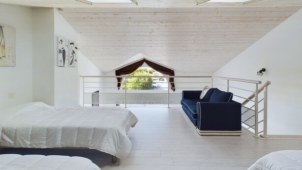 A spacious room with a high ceiling, a balcony, and a view of greenery outside.