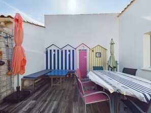 A patio with a wooden table and chairs, a bench, and colorful beach huts.