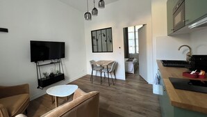 Un soggiorno moderno con una TV a schermo piatto, un tavolino rotondo e un divano. È presente un angolo cottura con un lavello e un piano di lavoro.