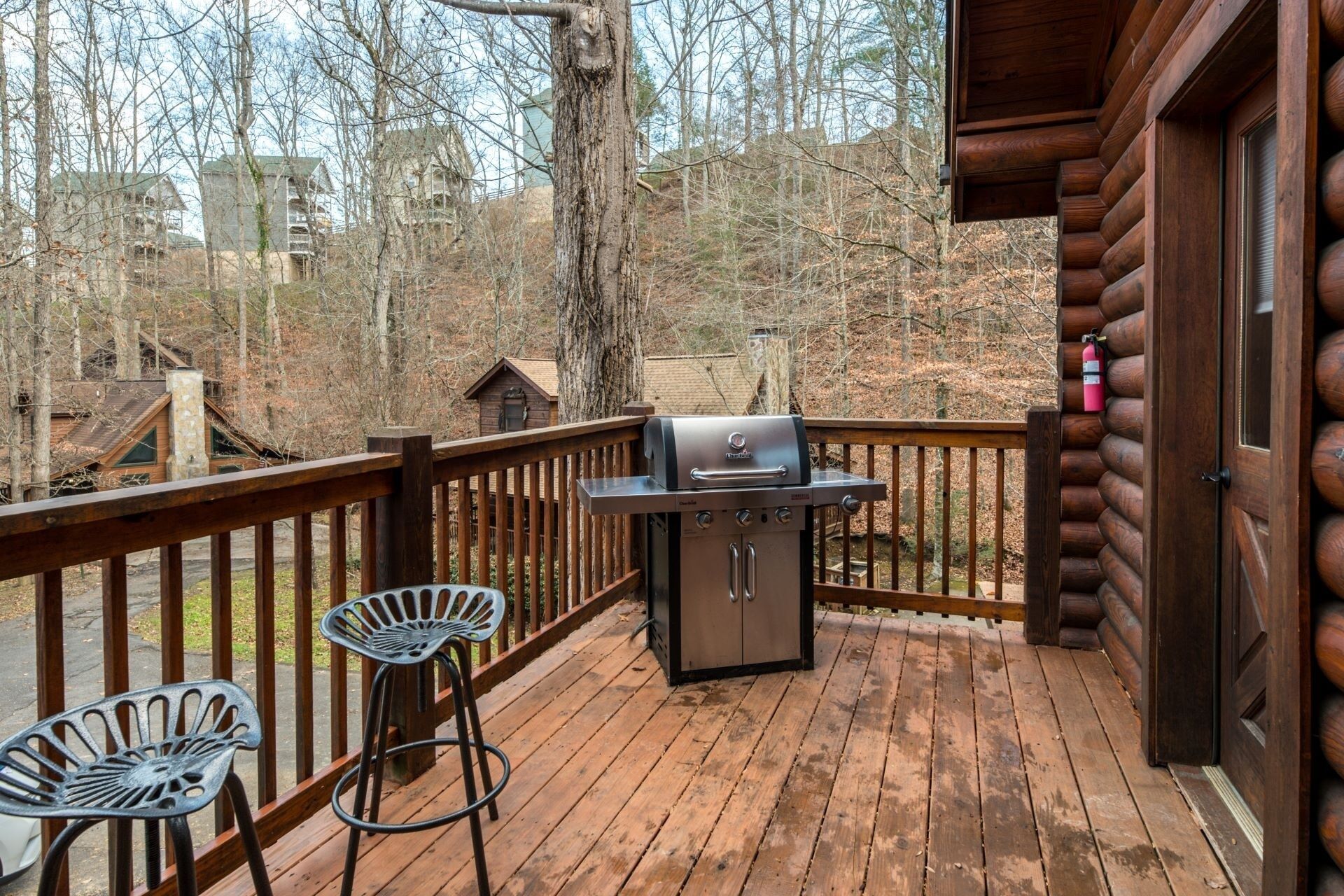 A wooden deck with a barbecue grill, a metal chair, and a wooden cabin structure.