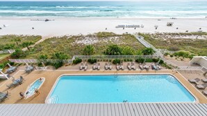 Un espace piscine doté de chaises longues et offrant une vue sur la plage et l’océan.
