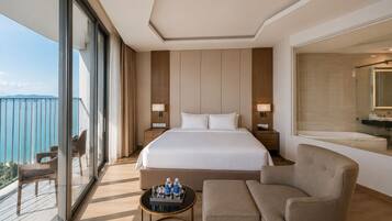 A hotel room with a large bed, two bedside tables with lamps, a sofa, a small round table with water bottles, and a balcony with a view.