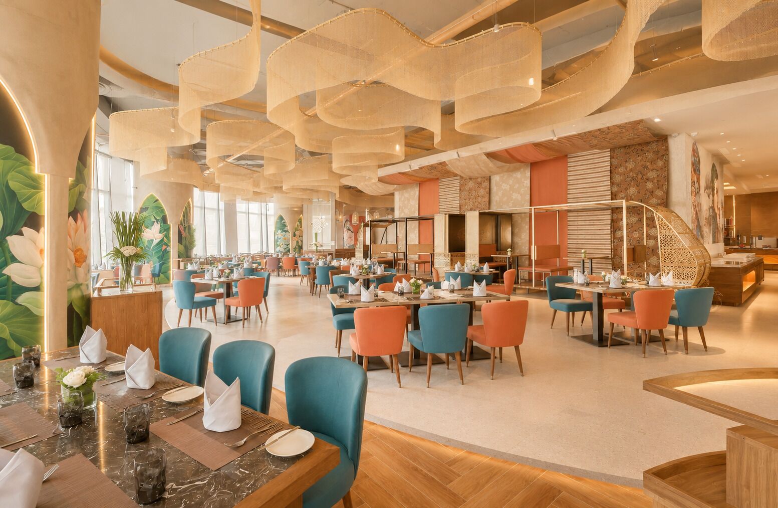 A spacious restaurant with multiple dining tables and chairs, a high ceiling with hanging light fixtures, and a mural on the wall.