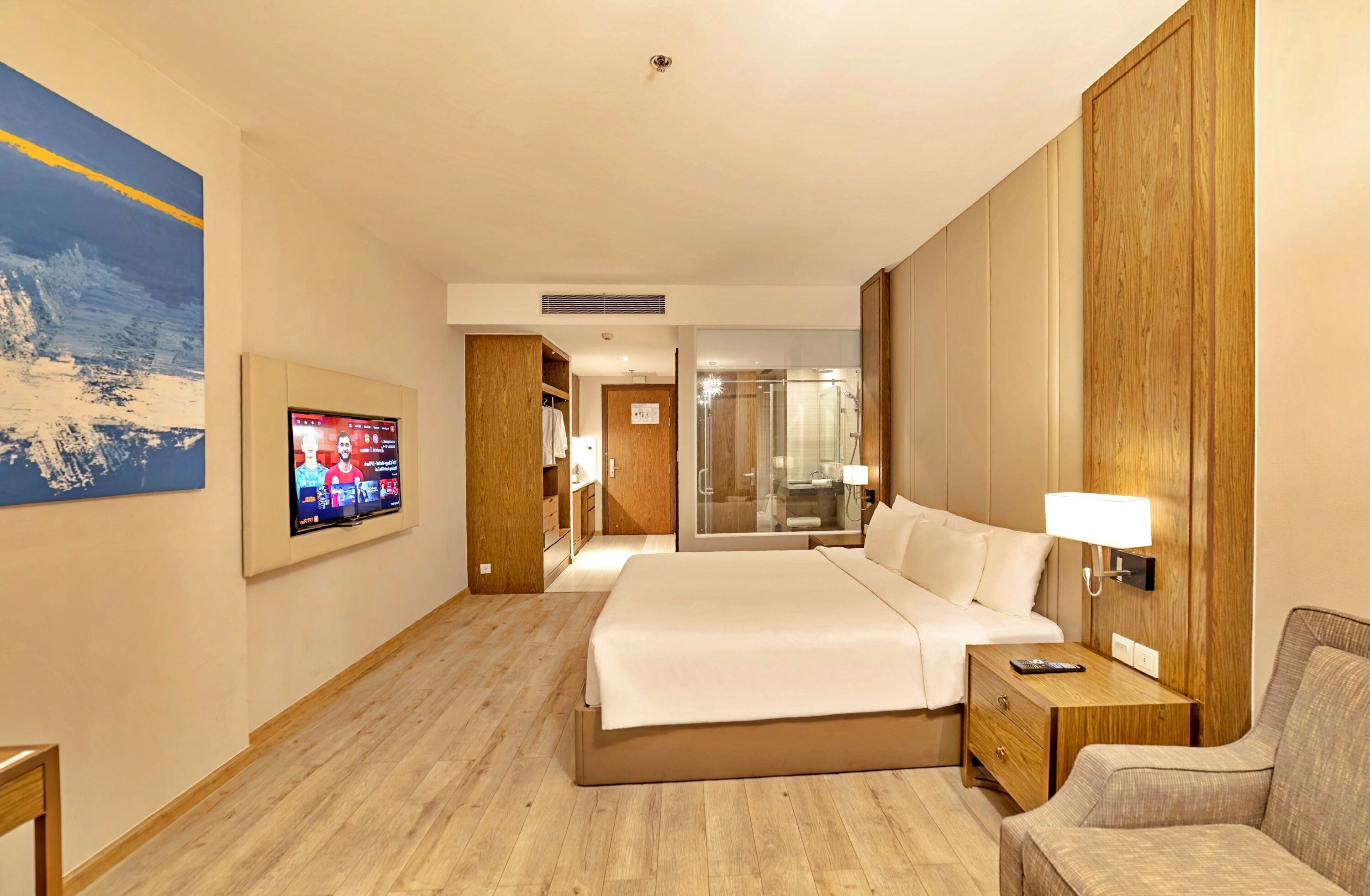A hotel room with a bed, a TV, a wooden wardrobe, a glass shower, and a sofa.