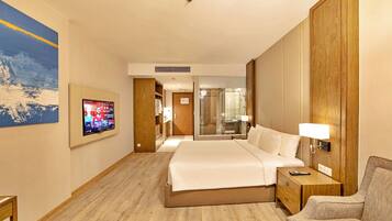 A hotel room with a bed, a TV, a wooden wardrobe, a glass shower, and a sofa.