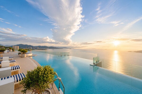 Une piscine à débordement offrant une vue sur l’océan et les montagnes, des chaises longues et des plantes en pot.