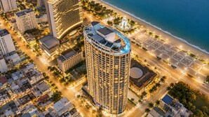 A high-rise hotel with a rooftop pool, adjacent to a beach and a busy street.