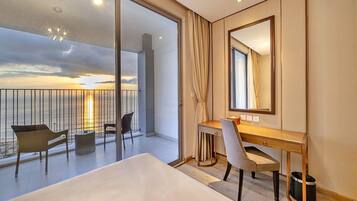A hotel room with a balcony, a desk, a chair, and a large mirror.