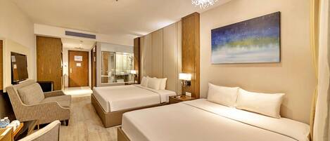 A hotel room with two beds, a sofa, a TV, and a painting on the wall.
