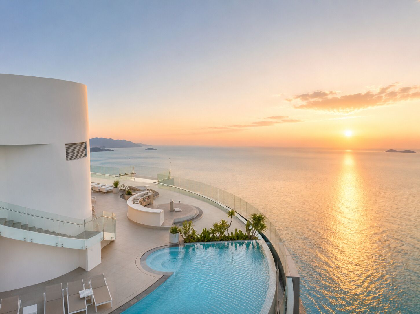 A poolside area with a view of the ocean at sunset, a curved pool, and a modern building structure.