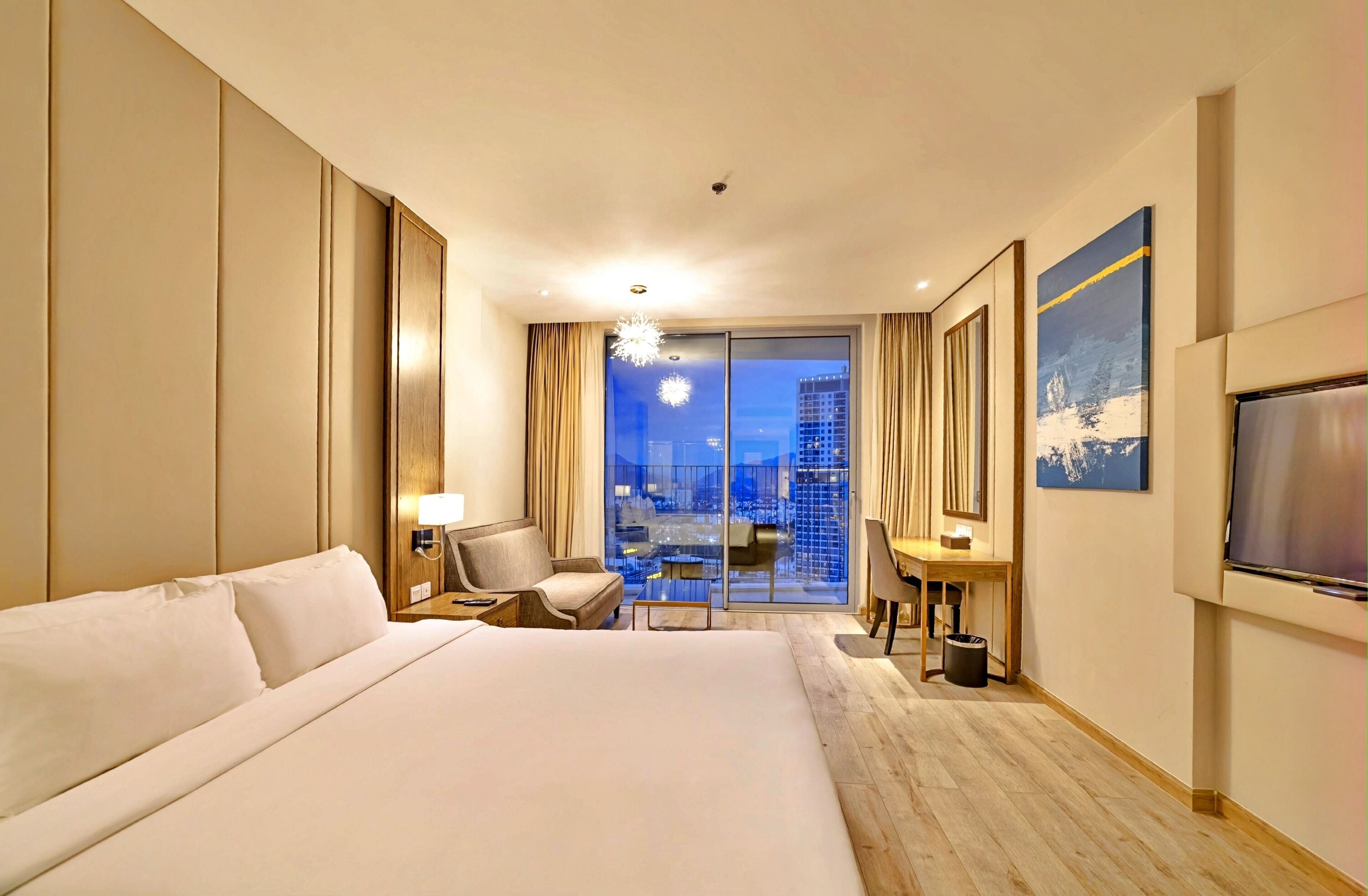 Habitación de hotel con una cama grande, un escritorio, una silla, un televisor y vistas a la ciudad.