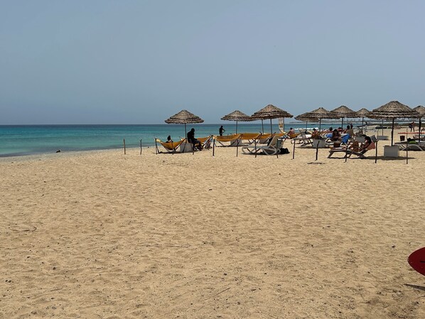 A beach with thatched umbrellas and sun loungers.