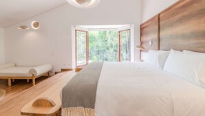 A modern bedroom with a large bed, a wooden headboard, a bedside table, and a view of greenery through a bay window. - w Incredible 5BR House w Jacuzzi in El Poblado (Medellín)