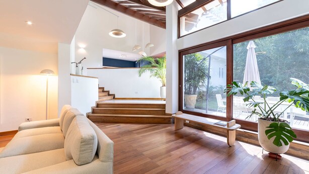 A modern interior with wooden floors, a staircase, a sofa, and large windows offering a view of the outdoors. - w Incredible 5BR House w Jacuzzi in El Poblado (Medellín)