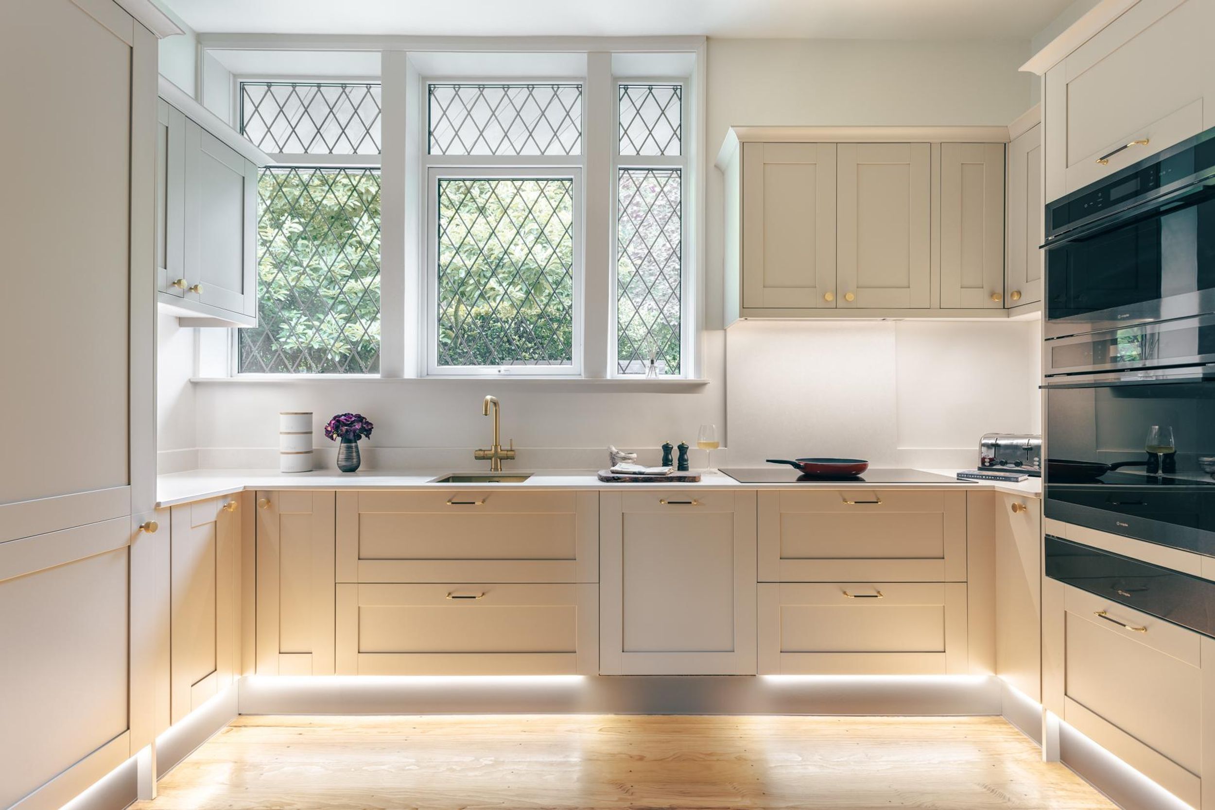 Een moderne keuken met witte kasten, een dubbele spoelbak en een groot raam met uitzicht op groen.