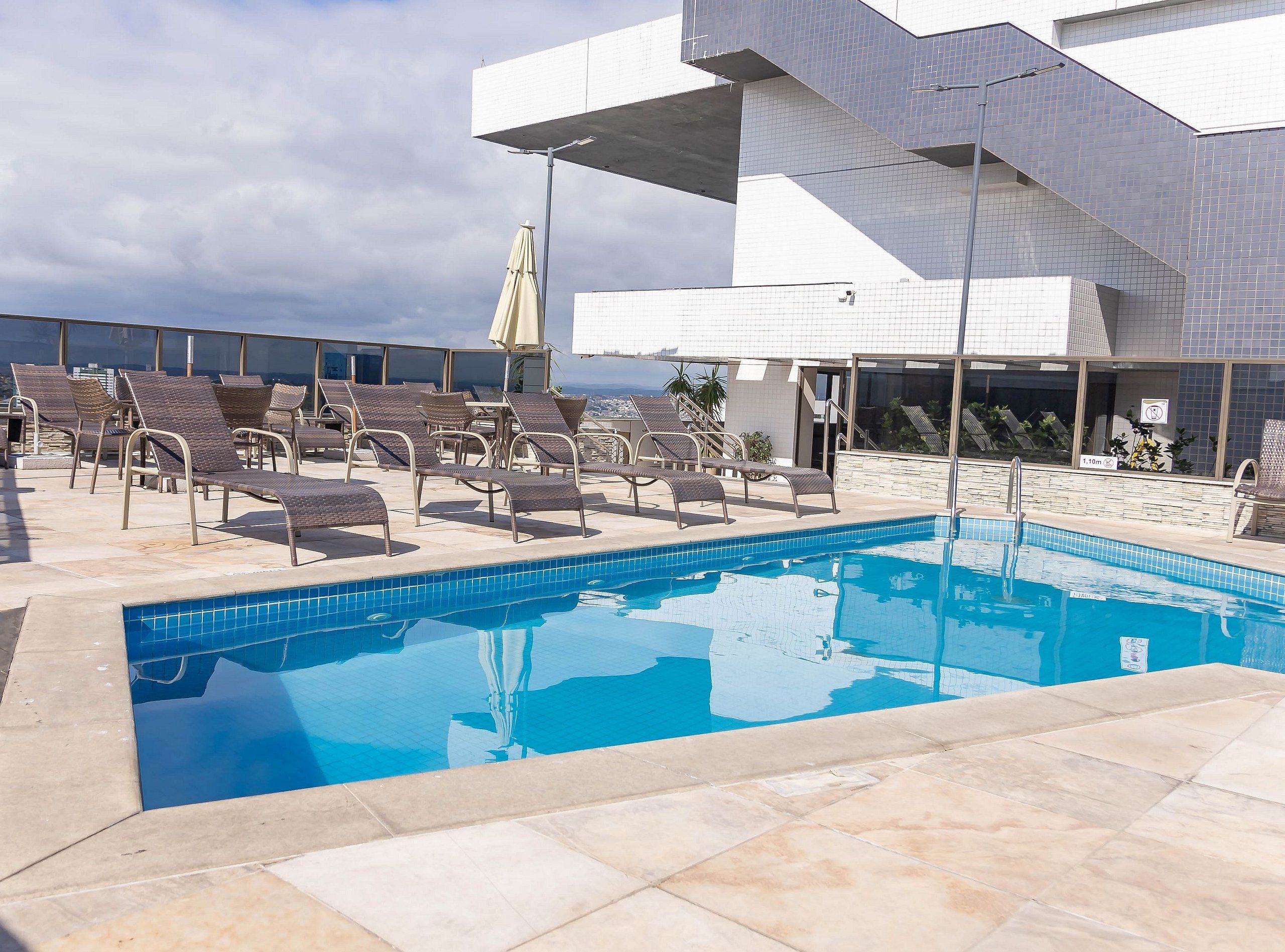 Uma piscina no terraço com espreguiçadeiras, vista desobstruída da cidade e um edifício moderno com paredes revestidas de azulejos.