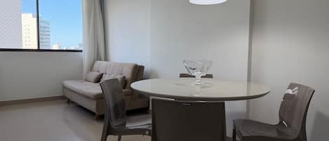 A modern room with a round table, two chairs, a sofa, and a hanging light fixture.