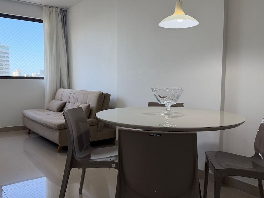 A modern room with a round table, two chairs, a sofa, and a hanging light fixture.