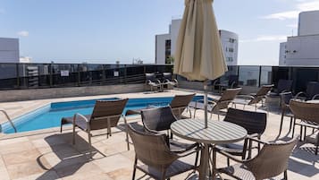 Área de piscina no terraço com cadeiras e mesas de vime, piscina e vista para a cidade.