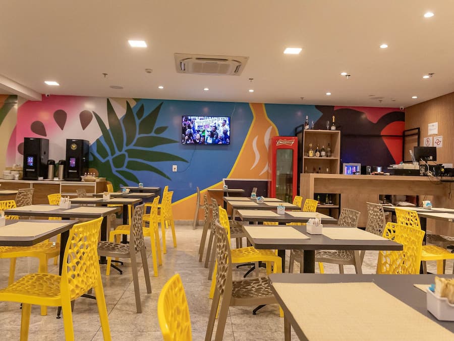 Un restaurant avec des tables et des chaises, un téléviseur fixé au mur et un réfrigérateur rempli de Coca-Cola.