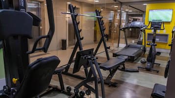 Une salle de sport équipée de matériel d’exercice, d’un tapis de course et d’un écran de télévision diffusant un événement sportif.